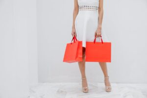 Woman in a white dress holds orange shopping bags, showcasing fashion and style.
